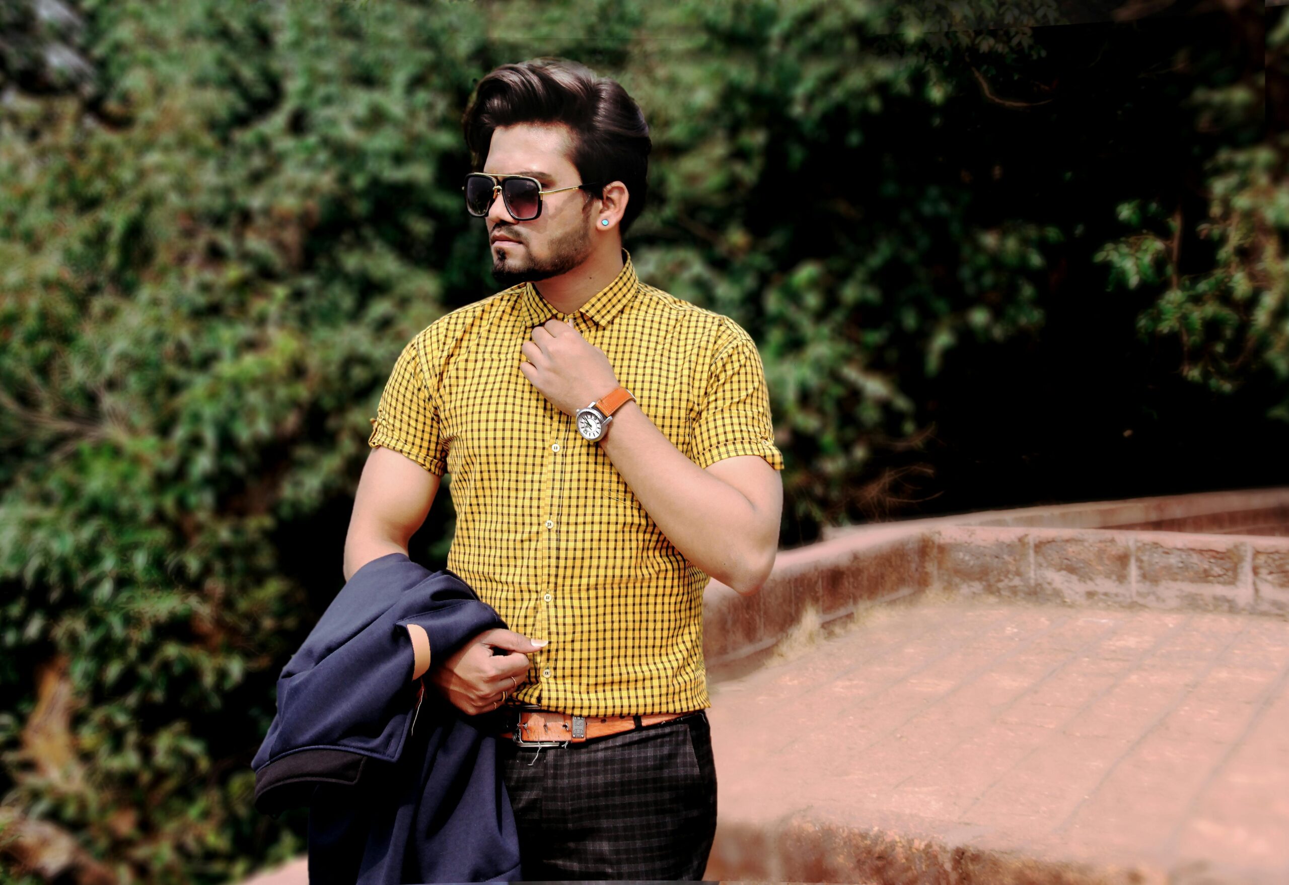 Stylish man wearing sunglasses and checkered shirt posing outdoors in Mahabaleshwar.