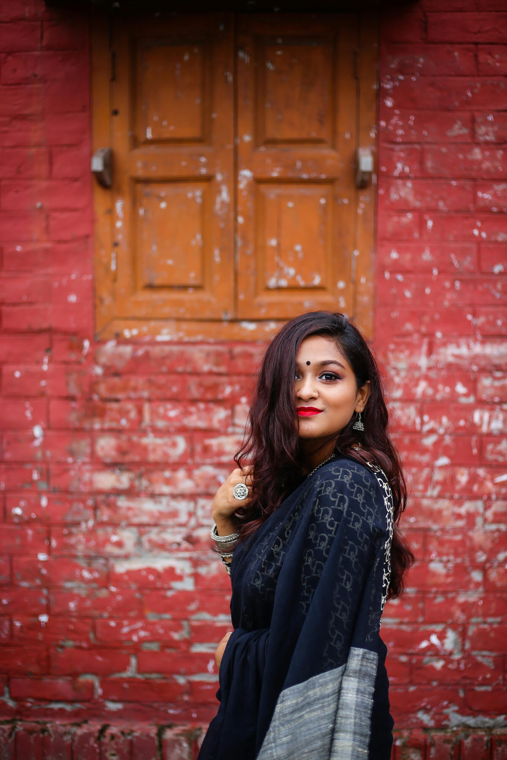 Charming woman in traditional attire posing against a rustic brick wall, showcasing elegance and cultural heritage.